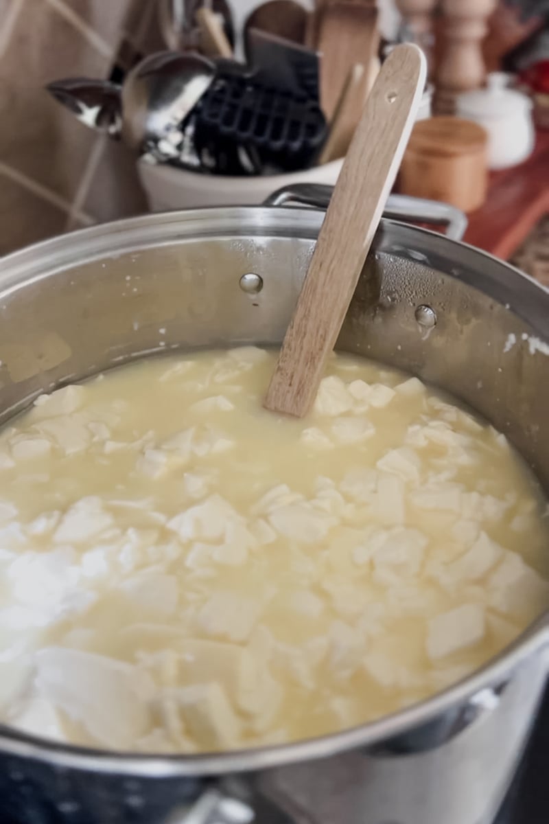 Heating homemade cheddar cheese curds in a large pot during the cheesemaking process.