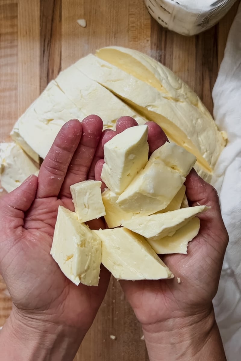 Hands holding cheese curds that have been cut into 1" pieces.