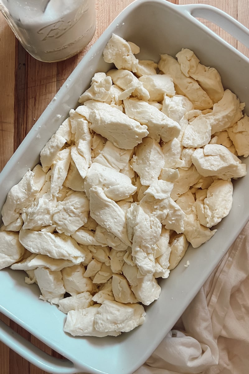 Fresh homemade cheddar cheese curds in a white baking dish on a wooden cutting board.