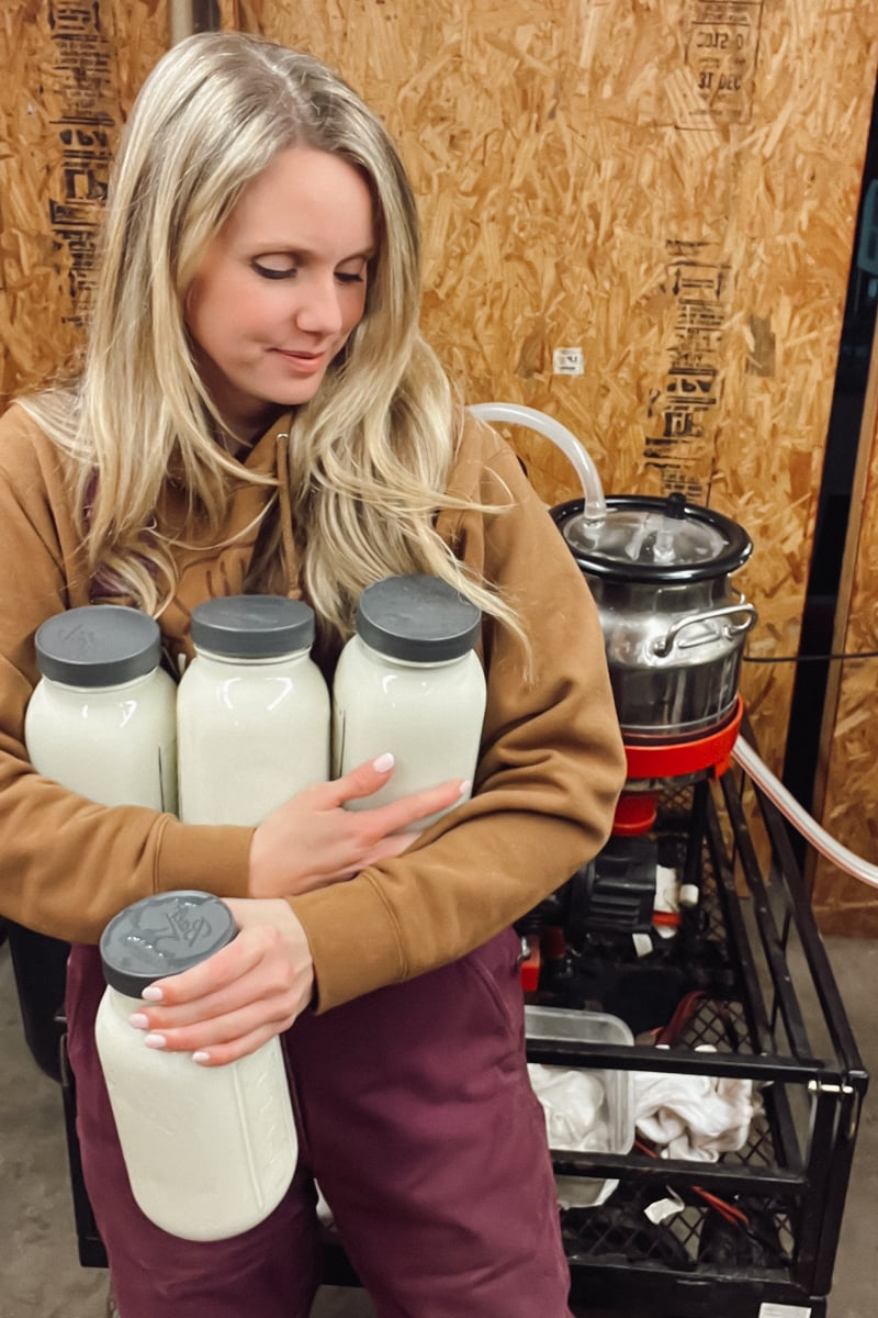 Meg holding jars of fresh raw milk in her homestead milk room, used for cheesemaking.