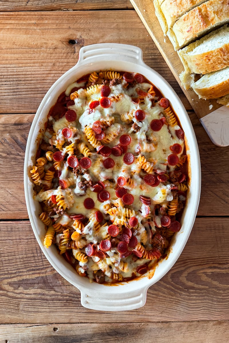 Overhead view of a homemade pizza pasta bake topped with melted mozzarella cheese and mini pepperoni in a baking dish.