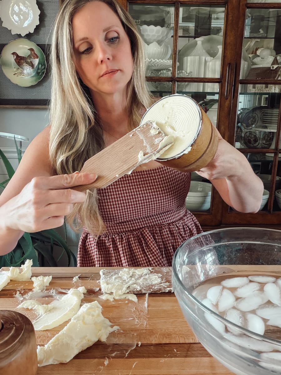 Packing cold homemade butter firmly into an antique wooden butter mold with a butter paddle.